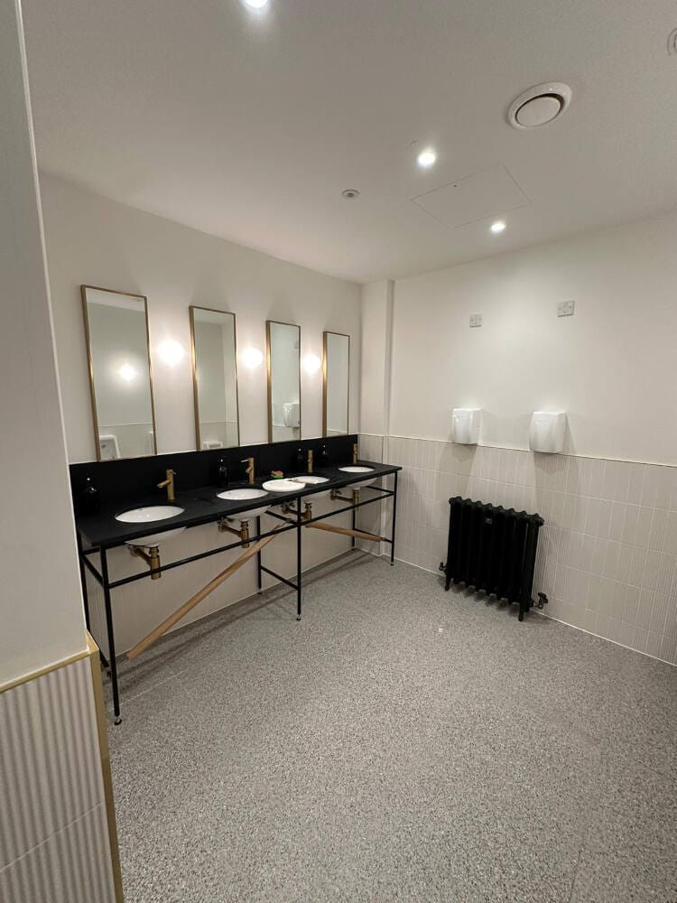 A refurbished commercial washroom with brass-framed mirrors and wall lighting installed by Coutts Electrical